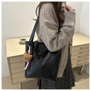 Detail of black leather tote bag featuring a cute brown plush bear charm and striped ribbon