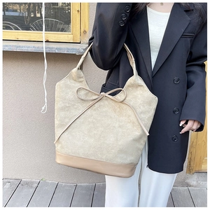 Detail of suede tote bag with bow accent and smooth leather base shown outdoors
