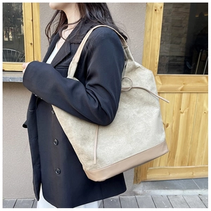 Detail of canvas tote bag featuring brown leather trim and side drawstring accents