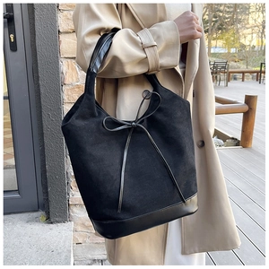 Close-up of black suede tote bag with leather bow detail and contrasting textures