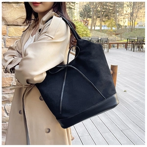 Detail of a large black suede tote bag with a bow accent shown in an outdoor lifestyle setting