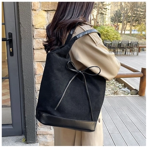 Detail of black suede tote bag with leather bow decoration on a beige trench coat