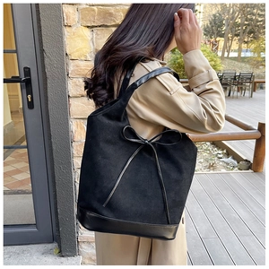Detail of black faux suede tote bag with leather bow on model in outdoor setting