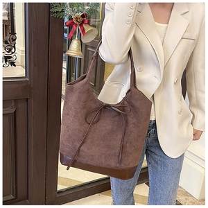 Close-up of a large coffee-brown faux suede tote bag with bow detail and leather base