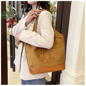 Close-up of brown suede tote bag featuring contrasting leather base and bow detail