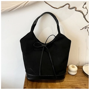 Detail of black fabric tote bag with leather strap and decorative bow knot on wooden desk