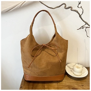 Close-up of brown suede hobo bag with bow detail on a rustic wooden table setup