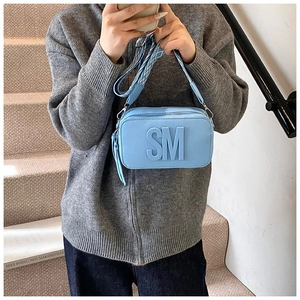 Detail of light blue crossbody bag with SM logo embossed and wide geometric strap