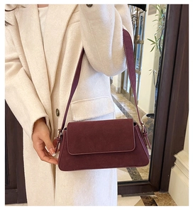 Close-up of a burgundy suede baguette bag worn with a white coat for a stylish look