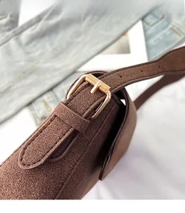 Detail of adjustable long shoulder strap with gold metal buckle on brown matte handbag
