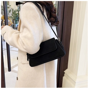 Side view of black matte underarm bag with adjustable strap worn on beige coat