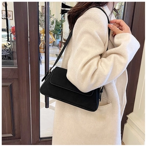 Detail of a black matte underarm bag worn by a model in a stylish beige wool coat