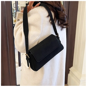 Detail of minimalist black baguette bag featuring matte leather and golden buckle