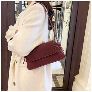 Side view of a vintage wine red suede baguette bag worn on a cream wool coat