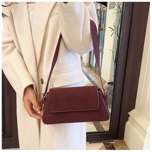 Close-up of burgundy suede baguette bag with gold hardware and wide shoulder strap