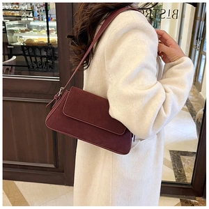 Model wearing a burgundy suede baguette bag with gold buckle in a bistro setting