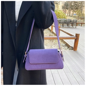 Close-up of a purple suede underarm bag with metal buckle shown on a model