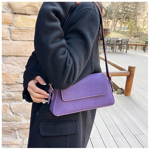 Detail view of purple suede baguette bag with a metal buckle on an outdoor shoulder strap