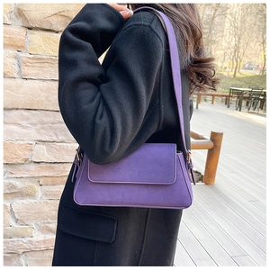 Close-up of purple faux suede baguette bag with slim shoulder strap and flap closure