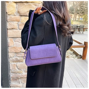 Detail of purple suede baguette bag worn with black wool coat on an outdoor terrace