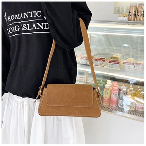 Brown suede baguette bag worn on shoulder with broad strap and gold hardware accents