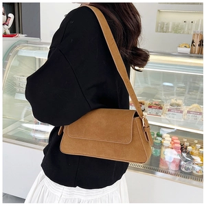 Close-up of brown suede baguette bag with adjustable strap worn on the shoulder