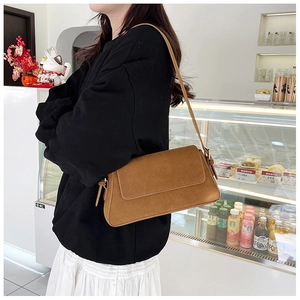 Brown faux suede baguette bag with slim shoulder strap shown in a cozy cafe setting