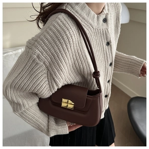 Detail of a dark brown leather shoulder bag with a gold cross lock and knot strap