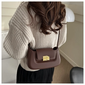 Chocolate brown leather baguette bag with unique gold metallic buckle on a beige sweater