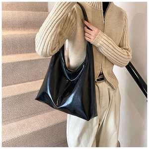 Vista laterale di una borsa hobo nera lucida indossata da una modella in interno