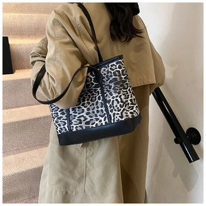 Detailed view of leopard print tote bag with black trim worn with a khaki trench coat