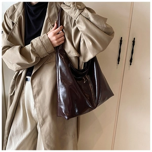 Close-up of a large glossy chocolate brown tote bag worn with a stylish trench coat