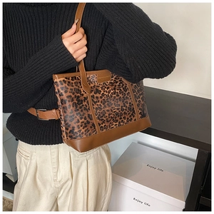 Detail view of leopard print tote bag featuring brown leather trim and fashion patch