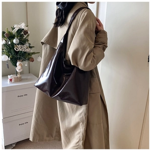 Detail of dark brown glossy hobo bag in large capacity worn with a classic trench coat