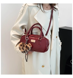Detalle de bolso cilíndrico rojo oscuro brillante con colgante de corazón y placa metálica
