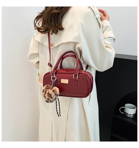 Detalle de bolso bandolera rojo oscuro con hebilla dorada y dije de leopardo en gabardina
