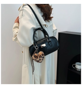 Detalle de bolso negro cilíndrico con colgante de corazón de leopardo y herrajes dorados