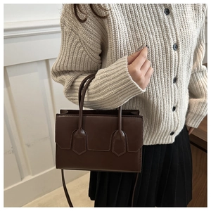 Detail of dark brown leather handbag with adjustable strap worn by a model in casual outfit