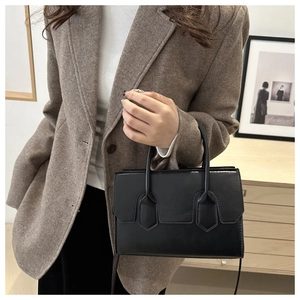 Detail of a minimalist black leather tote bag featuring shield-shaped stitching and dual handles