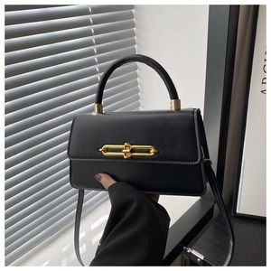 Detail of matte black crossbody bag with gold chain lock and top handle held by hand