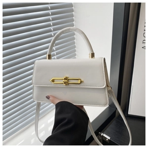 Detail of white patent leather handbag with gold chain buckle and top handle in soft lighting