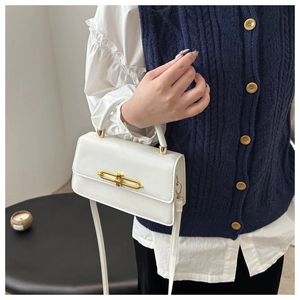 Detail of white leather crossbody bag with golden rectangular buckle on blue vest