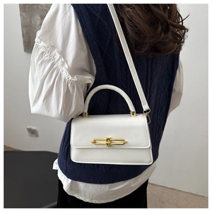 Detail of white leather crossbody bag with gold metal clasp on navy knitted vest