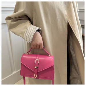 Detail of a rose red crossbody bag featuring gold horseshoe buckle and smooth leather