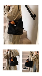 Black large capacity tote bag with plush teddy charm shown on a khaki trench coat