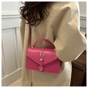 Detail of magenta faux leather crossbody bag with gold buckle on a beige coat outfit