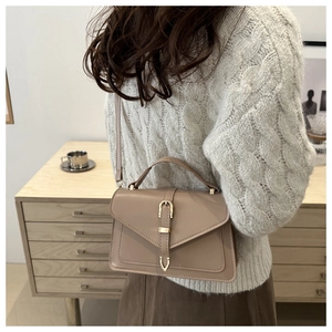 Detail view of khaki leather crossbody bag with metal buckle on a cozy knit sweater