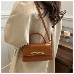 Detail of caramel brown crossbody bag with gold metal clasp on beige trench coat