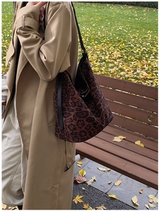 Detail of a large leopard print hobo bag worn with a classic khaki trench coat outdoors