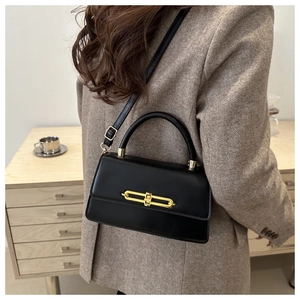 Close-up of elegant black crossbody bag featuring a sleek gold metal bar lock on the flap